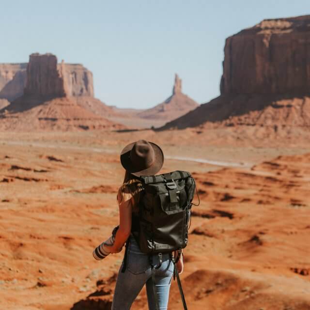 woman with black backpack standing on brown dessert